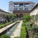 3 people in a courtyard filled with plants, trees and a stream flanked by fountains